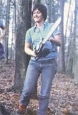 A young woman grins with satisfaction after cutting her first log with a chain saw.